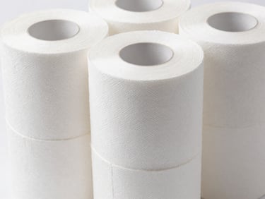 Macro close-up of a stack of large, commercial-grade tissue paper rolls, uniformly white, bright clinical studio light, sterile white background.