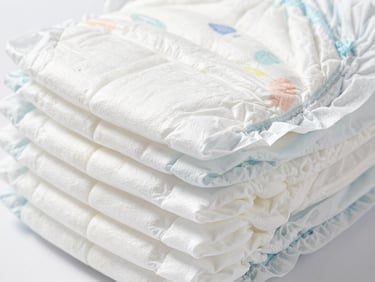 Cross-section of a multi-layer baby diaper showing absorbent core, sterile white and cool gray tones, macro lens
