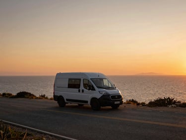 A sleek compact campervan parked on a narrow coastal road overlooking the sea at sunset, warm cinematic tones, wide angle