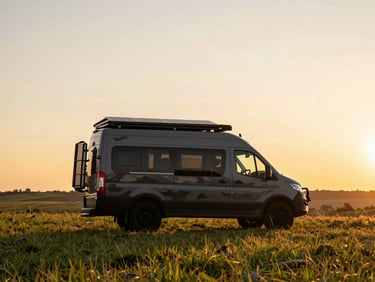 Custom off-road Multicamper van parked on a remote grassy hill, solar panels visible on the roof, rugged terrain in background, sunset light