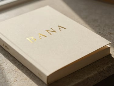 A minimalist book cover with gold foil lettering on a warm cream background, resting on a stone surface, soft shadows.