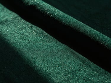 Macro close-up of textured emerald fabric under dramatic high-contrast studio lighting, warm shadows, 35mm film grain.
