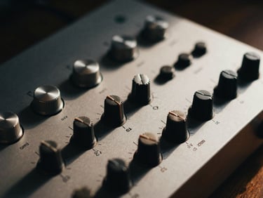 Close-up of sleek audio hardware dials on a warm wooden surface, deep natural shadows, cinematic editorial lighting.