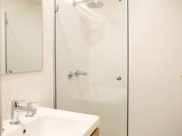 Bright, clean attached bathroom with modern white fixtures, sparkling chrome taps, and spotless glass shower area