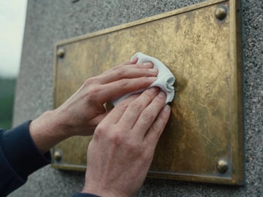 Hands gently cleaning a weathered brass plaque on a monument, soft overcast daylight, desaturated tricolor tones, deep shadows, 35mm film grain