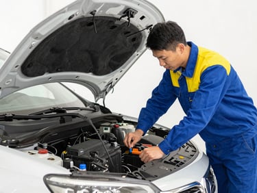Technician opening the hood of a car to check the battery, bright workshop lighting, medium shot, high-contrast blue and yellow tones, 35mm lens.
