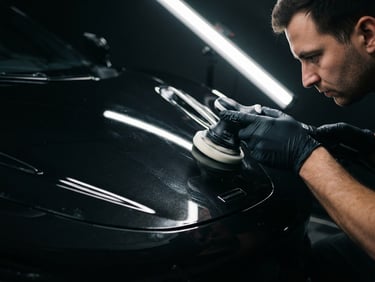 Close-up of a specialist correcting paint under sharp overhead LED inspection lights, showcasing a perfect reflection line on deep metallic black paint, 50mm lens