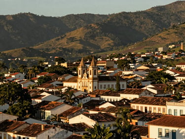 Wide panoramic shot of a historic Brazilian town nestled in green mountains, warm golden hour sunlight, architectural heritage, negative space, 35mm lens