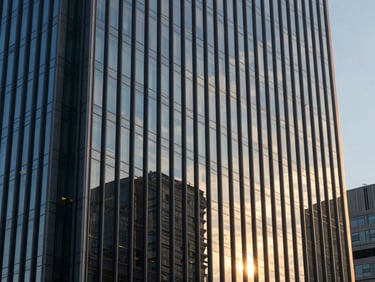 Vista abstrata de um edifício corporativo moderno, com reflexos de luz em suas fachadas de vidro azul-marinho ao pôr do sol, focando em linhas arquitetônicas nítidas. Sem pessoas.