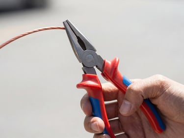 Close-up of hands gripping high-leverage red and blue combination pliers cutting thick copper wire