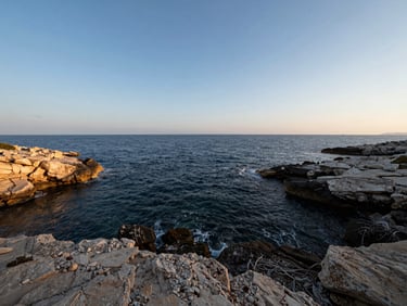 Wide panoramic 21:9 framing of an untouched coastal plot on the Adriatic shoreline, deep navy water meeting raw limestone, expansive sky, soft Mediterranean morning light.