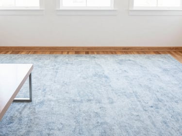 A bright, airy living room with a perfectly vacuumed carpet, dust-free wooden baseboards, and polished coffee table reflecting natural light. High-key natural daylight.