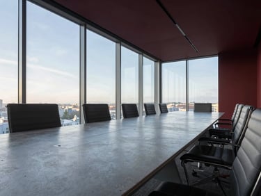Low-angle perspective of a modern executive boardroom with a long polished concrete table, minimalist chairs, and floor-to-ceiling glass windows, morning light