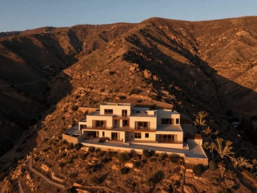 Drone shot of Sacred Valley at golden hour, low-profile modern villa integrated into the mountain, warm earth tones, dramatic shadows.