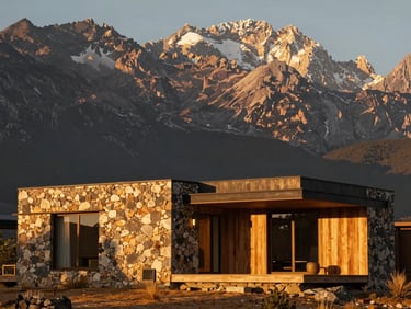 A modern minimalist villa made of local stone and eucalyptus wood, nestled against a towering Andean mountain face, dramatic golden hour shadows, warm architectural lighting