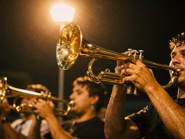 Dynamic low-angle shot looking up at a gleaming brass horn section, sweat glistening on musicians under warm golden streetlamp glow, motion blur, 35mm film style.