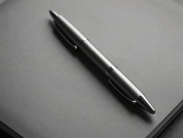 Detail of a brushed steel pen on a leather notebook, high contrast, diffused light, monochrome.