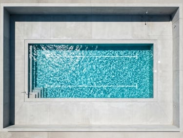 Top-down architectural shot of a minimalist rectangular swimming pool, bright midday sun reflecting off sparkling turquoise water, sharp geometric concrete lines, 35mm lens