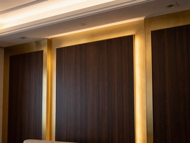 A close-up of a luxury Riyadh living room wall featuring brushed champagne gold trim and dark wood paneling, warm architectural LED lighting, 35mm lens