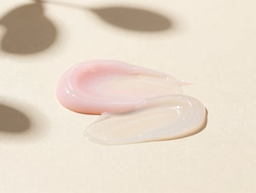 Macro shot of two different skincare product textures (gel and cream) layered on a glass surface, soft shadows of botanical leaves, luminous editorial photography.