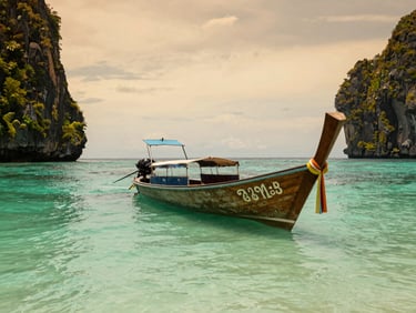 A longtail boat anchored in crystal clear turquoise water near limestone cliffs in Thailand, golden sunset light, 35mm