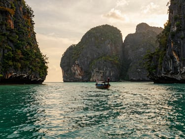Scenic limestone cliffs rising from turquoise water in Phang Nga Bay, longtail boat in the distance, golden hour light
