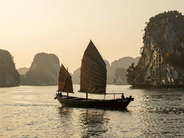 Traditional wooden junk boat sailing slowly through calm misty waters of Halong Bay, warm golden light, 35mm