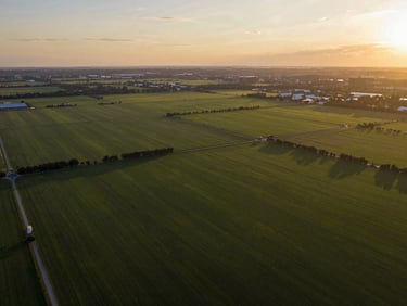 Professional high-altitude aerial drone view of expansive green investment land and acreage at golden hour.