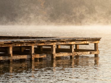 Deep-water dock construction on a calm misty lake, heavy timber cribbing visible, warm editorial photography.