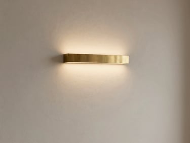 Minimalist concrete living room, soft warm light reflecting off a brushed brass wall fixture, gentle shadows, editorial interior photography