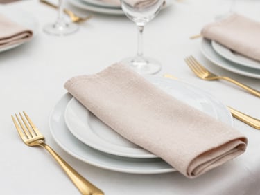 An elegant tabletop setting with gold cutlery, white ceramic plates, and delicate blush linen napkins, soft daylight, 35mm