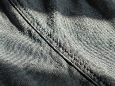 Macro close-up of bound garment seams on heavy Japanese raw denim, stark high-contrast side-lighting emphasizing the precise thread work, 35mm