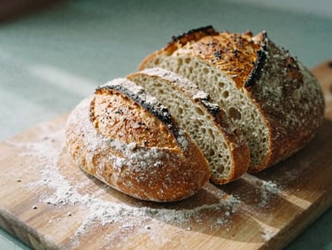 Close-up of freshly baked sourdough bread being sliced on a wooden board, flour dusting the air, warm shadows, 35mm film.