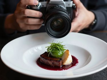 Close-up of a photographer's hands holding a camera, capturing a beautifully plated dish in a restaurant setting, moody Scandinavian daylight, high contrast, 35mm lens.