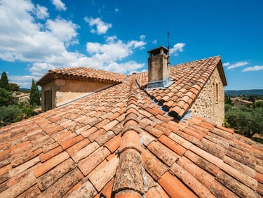 Low-angle shot of a restored terracotta tile roof in Provence under bright Mediterranean sunlight, deep blue sky, sharp clay textures