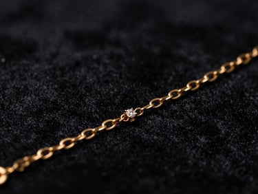 Close-up macro shot of a delicate gold bracelet with small diamonds, catching light, dark textured velvet backdrop, dramatic low-key lighting, deep black and gold tones, shallow depth of field
