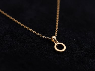 Close-up macro shot of a delicate gold chain necklace with a small pendant, draped on dark velvet, dramatic low-key lighting, deep black and gold tones, shallow depth of field