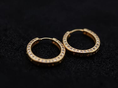 Close-up macro shot of a pair of elegant gold hoop earrings with small gemstones, dark textured backdrop, dramatic low-key lighting, deep black and gold tones, shallow depth of field