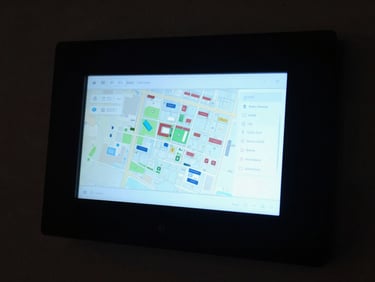Smart security panel interface lit by its own screen glow in a darkened room, touchscreen showing a property map, cool blue display light, surrounding darkness
