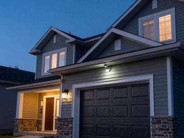 Exterior dusk shot of a suburban Nova Scotia home, a security camera mounted above a dark garage door, motion sensor visible near the front entrance, blue-hour sky, no warm light