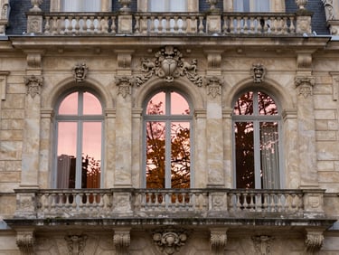 Close-up architectural detail of the Grand Hôtel or thermal palace in La Bourboule, intricate stone carvings, rose gold reflections on historic glass windows under soft autumn light.