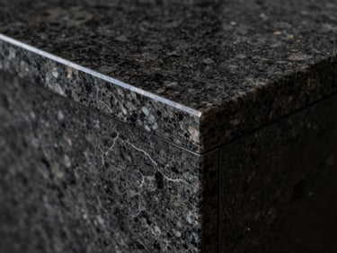 Extreme close-up of a flawless mitered joint (meia-esquadria) on a dark quartzite gourmet countertop, sharp directional lighting highlighting the seamless edge