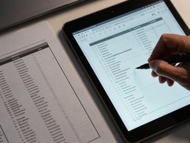 Overhead close-up of printed and digital documents side by side on a desk, a hand annotating a structured workflow report, cool directional light from above, visible file taxonomy labels and index tabs
