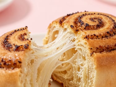 Macro shot of a soft cinnamon roll being pulled apart, showing the fluffy, steaming golden inner layers, warm natural light