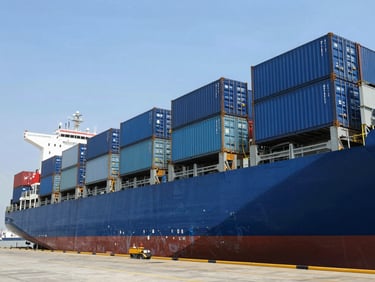 A wide-angle industrial shot of blue shipping containers being loaded onto a large cargo ship at Mundra port under bright, clear daylight, showcasing scale and logistics precision.