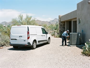 Wide shot of a clean, branded Established AC Solutions service truck parked in a desert driveway, an AC technician checking equipment in the background under bright midday desert sunlight, cool blue and metallic tones, sharp focus, 35mm lens