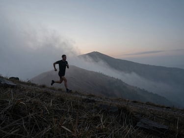 Wide cinematic shot of an athlete running on a misty mountain ridge at dawn, low-key lighting, cool atmospheric tones