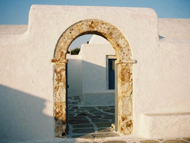 Medium shot of whitewashed stone archway in a quiet Greek village, soft natural shadows, warm side-lighting.