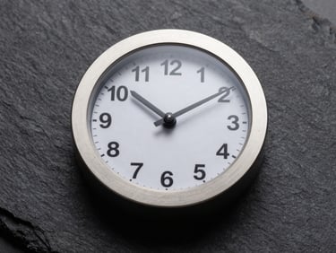 Macro flat-lay of a minimalist executive desk clock, brushed aluminum casing, sharp studio lighting, dark slate background, high contrast, landscape aspect