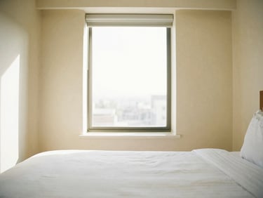 Bright, high-key photo of a clean hotel room interior with sun streaming through a large window, minimal design, optimistic tones, 35mm